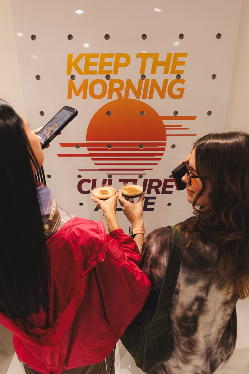 Duas amigas brindando na frente do painel Keep the morning culture alive