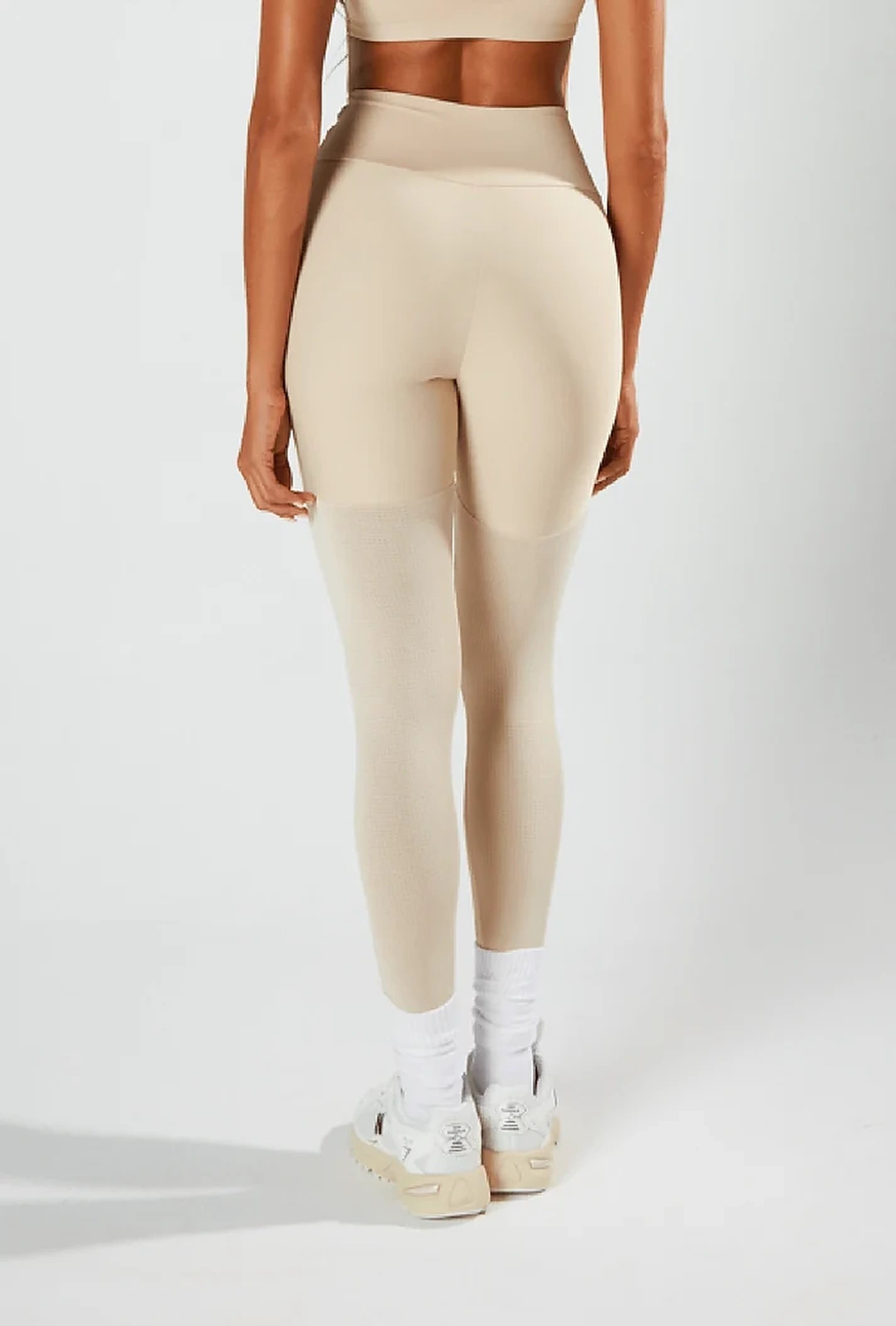 Modelo de costas com top e legging bege da linha Fresh+, com recortes perfurados nas pernas