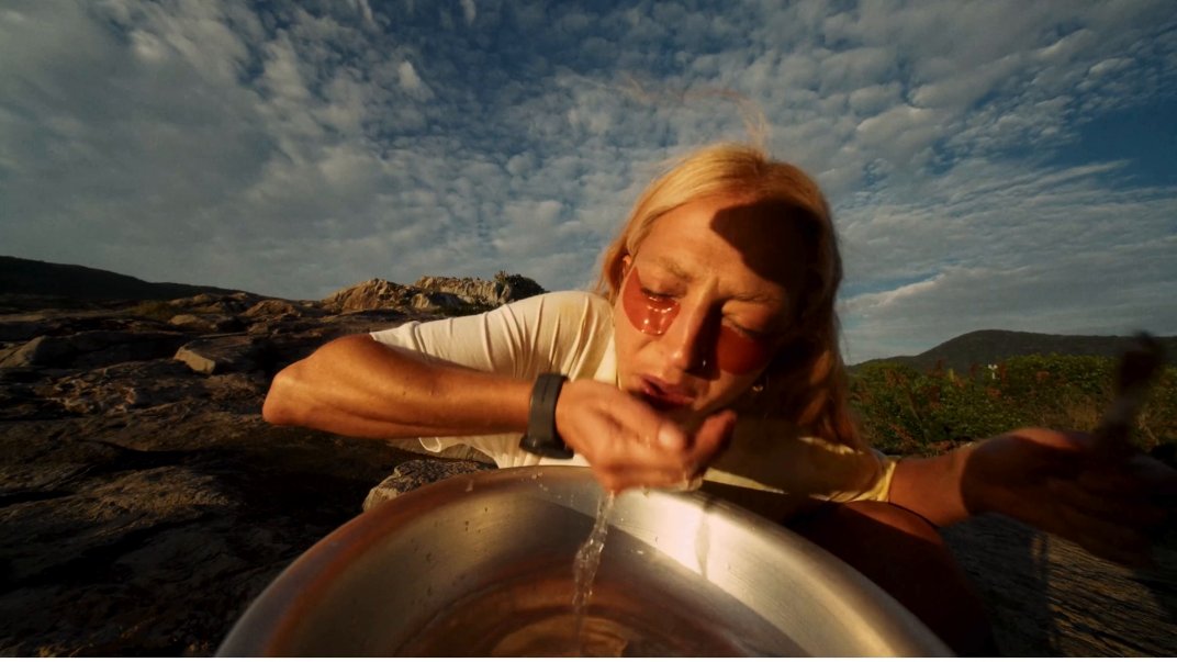 Mulher lavando o rosto numa bacia sobre as pedras